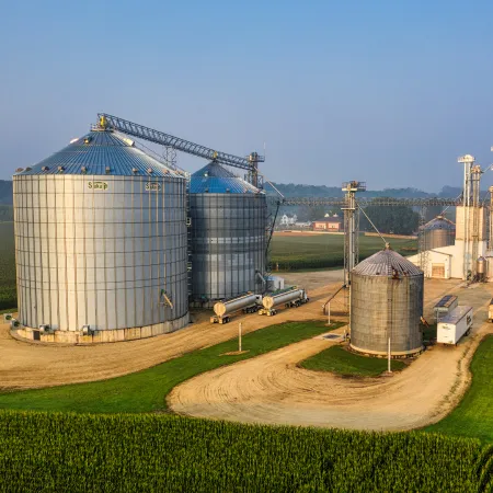 image showing huge grain storage silos surrounded by farm and a tanker loading area with tanker trucks