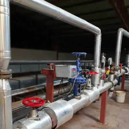 Best practices for temp and pressure systems An industrial piping system featuring a complex arrangement of silver-insulated pipes, blue and red valves, and a digital controller (likely for temperature or pressure), suggesting a hot fluid or steam transfer operation.