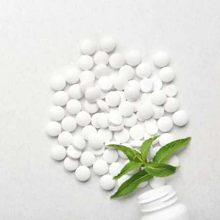 Malaysia Stevia White Stevia sweetener tablets piled on a white surface next to a mint sprig and a partially visible white bottle.
